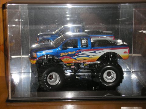 1995 Ford Bronco - A blue monster truck model with flame decals and sponsor logos is displayed in a clear case.