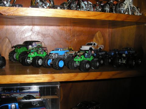 1995 Ford Bronco - Several monster truck toys are displayed on a wooden shelf, with other toys visible above and below.