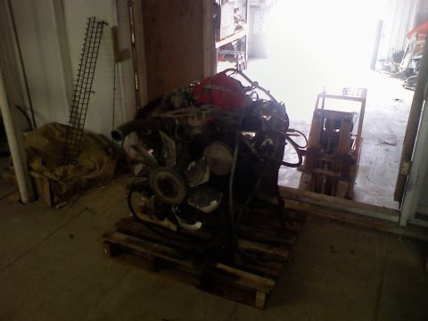 1979 Ford Bronco - Engine assembly sits on a pallet in a dimly lit warehouse, with a forklift visible in the background.