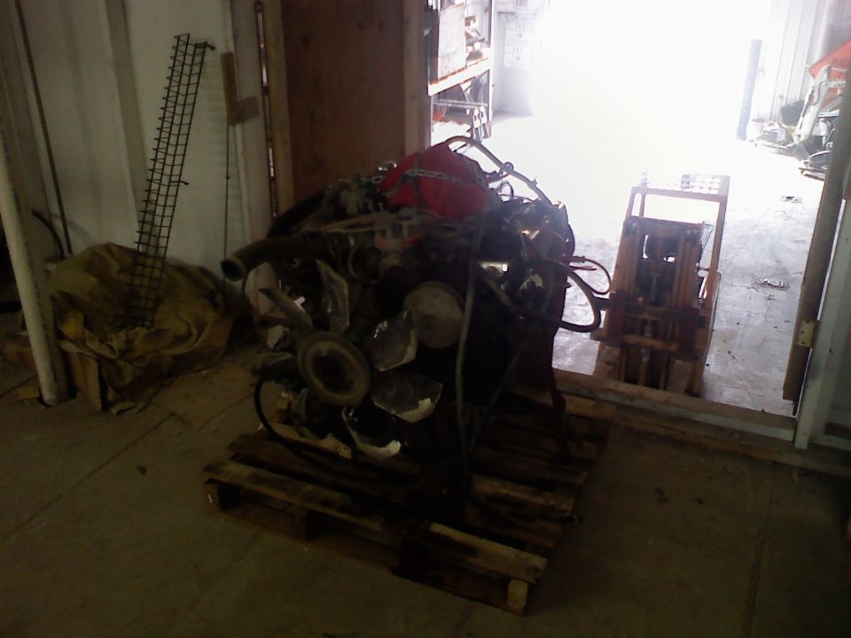 Engine on a wooden pallet, with a red tarp on top, in a warehouse setting
