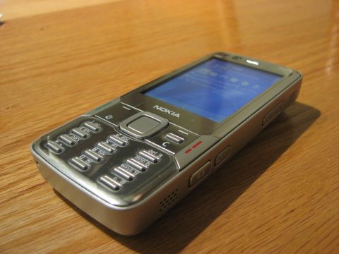 2003 Ford Crown Victoria - A silver Nokia cell phone rests on a wooden table, displaying a blue screen and its numeric keypad.