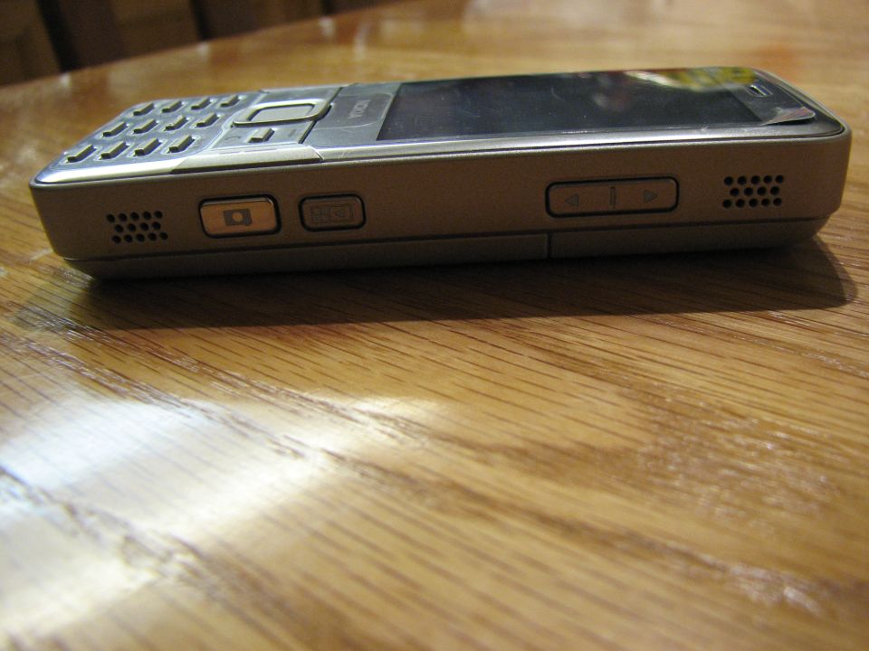 Silver Nokia phone on a wood table, low side-edge view showing keypad and side buttons