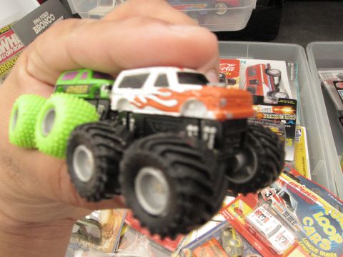 1986 Ford Bronco - A diecast monster truck toy with flame decals is held in a hand, with other toy vehicles in the background.