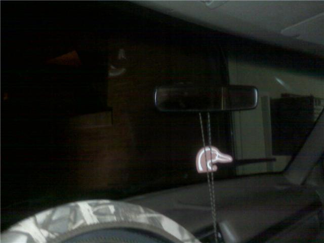 Interior view of a dark vehicle cabin, showing a rearview mirror and a duck-shaped air freshener