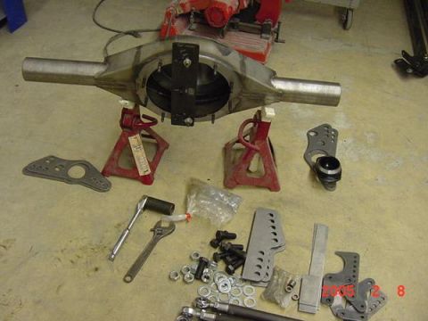 2007 Ford Mustang - A collection of parts for a rear axle assembly, including brackets, bolts, and tools, laid out on a concrete floor.