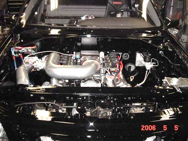 Black engine bay with chrome intake piping and visible engine components. Date stamp reads 2006 5 5