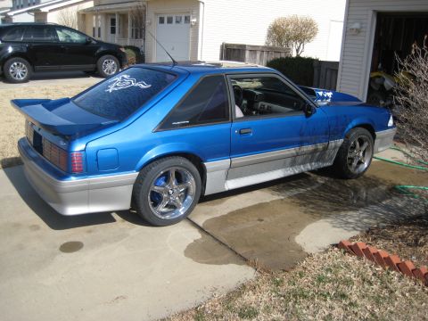 1990 Ford Mustang - A blue Ford Mustang is parked in a driveway next to a black SUV, with a garage door visible.