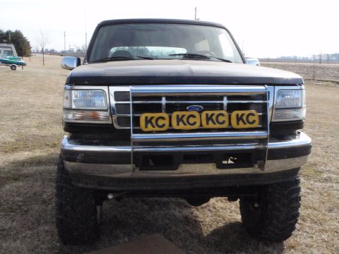 1996 Ford Bronco - Front view of a black Ford Bronco with four yellow KC lights mounted on the grille guard. The vehicle is parked outdoors on a dry grassy fi…