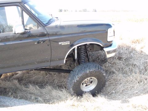 1996 Ford Bronco - The driver's side of a lifted black Ford Bronco is shown parked in dry grass. Visible mods include large off-road tires and suspension comp…