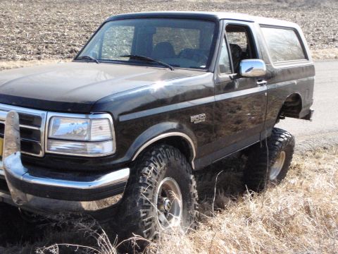 1996 Ford Bronco - A lifted black 1996 Ford Bronco is parked on a dirt road with dry grass and brush surrounding it. The front of the vehicle shows a chrome b…