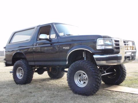 1996 Ford Bronco - A lifted black 1996 Ford Bronco with large off-road tires is parked on a grassy field. The front of the vehicle features a chrome bumper an…