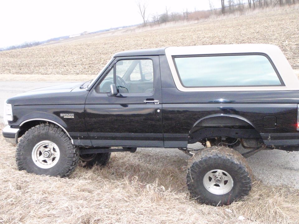Black 1996 Ford Bronco with tan roof and large off-road tires, side view.