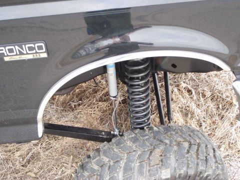 1996 Ford Bronco - Close-up view of the rear fender, suspension, and tire of a black Ford Bronco. A silver shock absorber and a silver coil spring are visible…