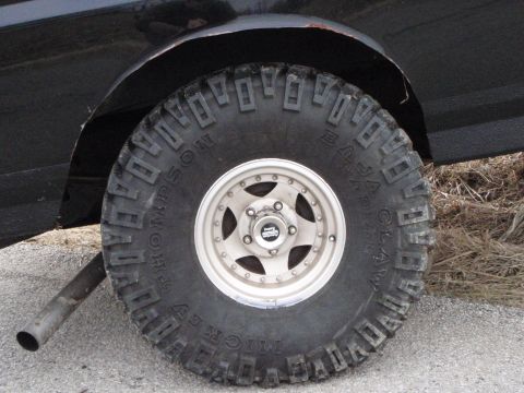 1996 Ford Bronco - A close-up view of a large, aggressive off-road tire on a black vehicle. The tire has prominent tread blocks and text that reads "MICKEY TH…