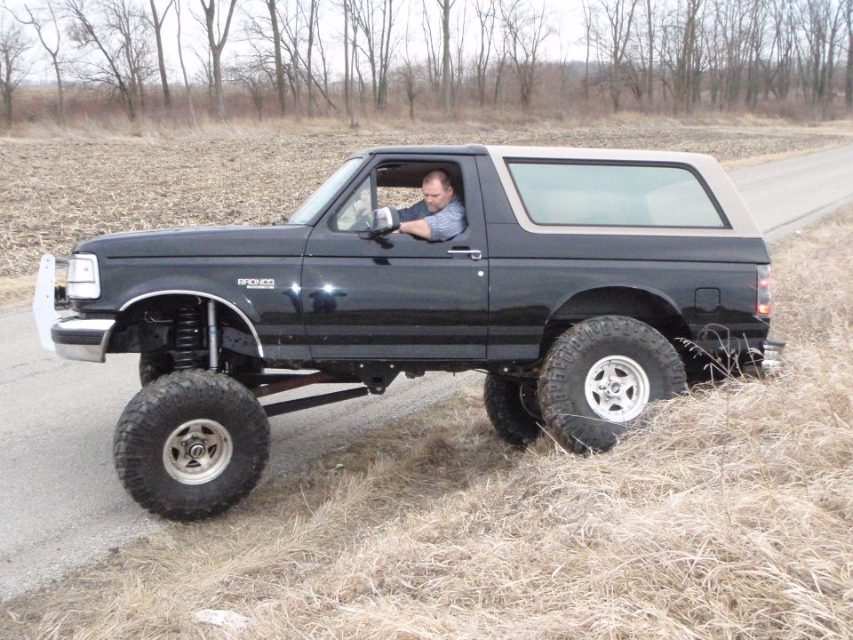 Lifted black 1996 Ford Bronco with tan roof on a dirt road.