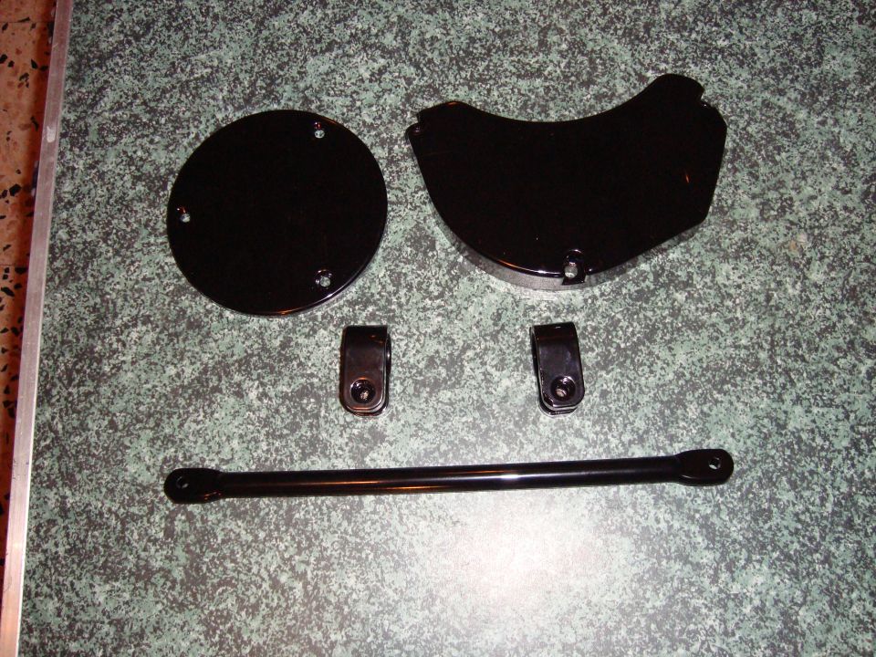Two black shiny car parts, a circle and a curve, with a bar and brackets on a speckled countertop.