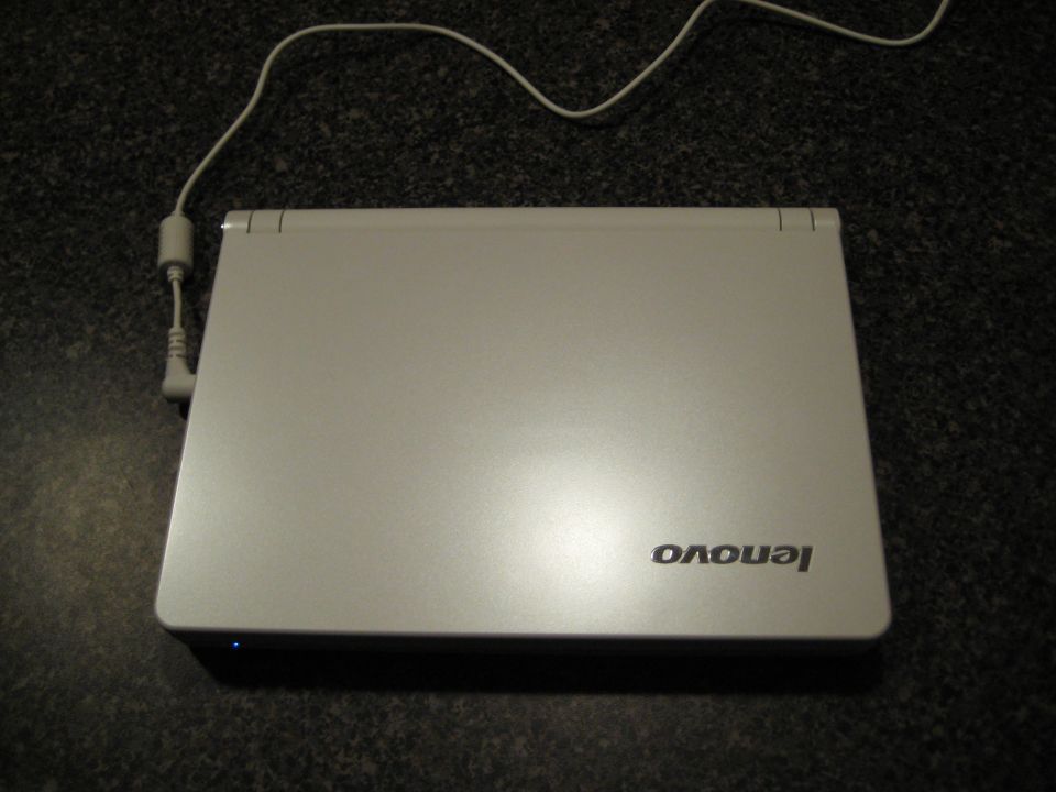 Closed silver Lenovo laptop with power cord plugged in.