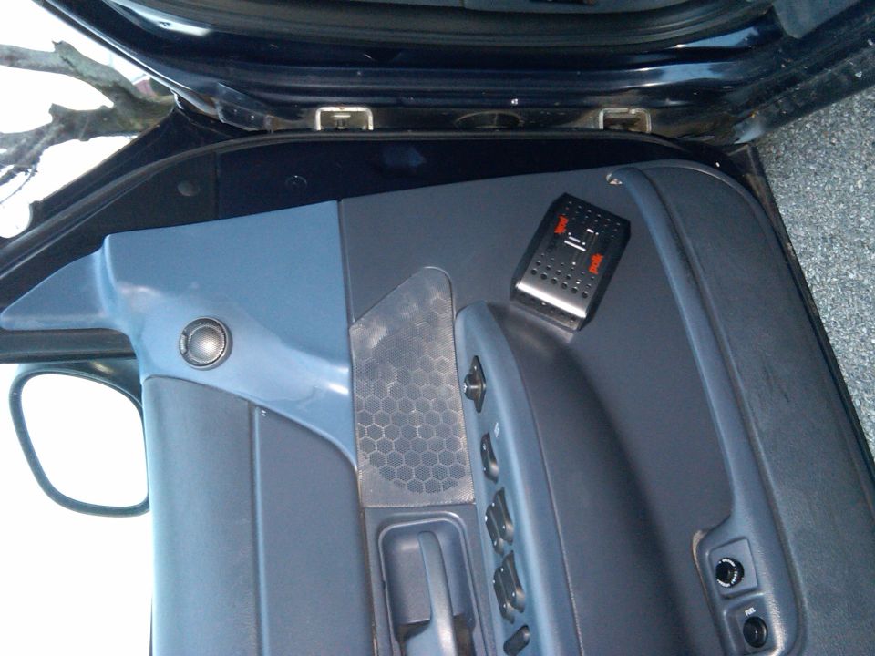 Gray door panel with Polk Audio crossover, aftermarket tweeter, and mesh speaker grille on an open car door