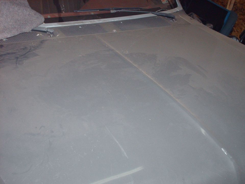 Dusty gray car hood with windshield wipers and a gray blanket on the cowl.