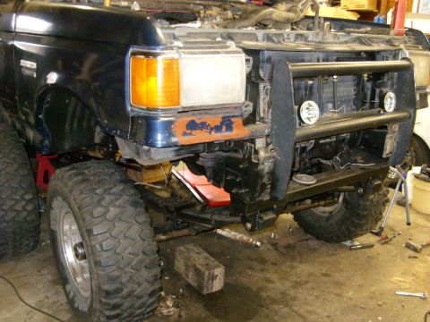 1988 Ford Bronco - The front driver's side of a dark blue Ford Bronco is shown, lifted with large off-road tires and a custom brush guard. The vehicle appears…