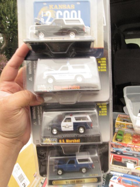 1986 Ford Bronco - A hand holds up a collection of three boxed die-cast model vehicles, two of which are Ford Broncos. The top box features a Kansas license p…