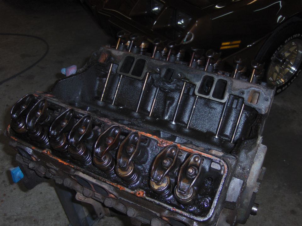 V8 engine block with rocker arms and pushrods visible, oily.