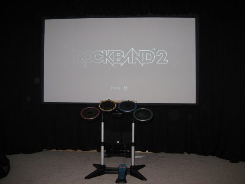 1979 Ford Bronco - Rock Band 2 game displayed on a projector screen with a drum set setup.