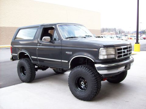 1992 Ford Bronco - A dark gray 1992 Ford Bronco is parked outside, a lifted suspension and aggressive tires.