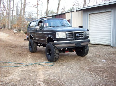 1992 Ford Bronco - This lifted 1992 Ford Bronco is shown in a three-quarter front view, parked on a gravel surface next to a building.
