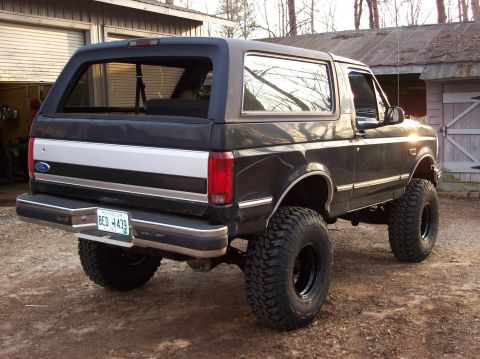 1992 Ford Bronco - This lifted 1992 Ford Bronco is parked outdoors near a garage and trees.