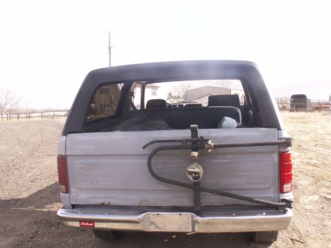 1986 Ford Bronco - The rear of a light-colored Ford Bronco shows a spare tire carrier and a red 'Edelbrock' sticker on the bumper.