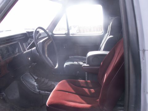 1986 Ford Bronco - The interior of a truck shows red velour seats, a steering wheel, and a floor shifter.