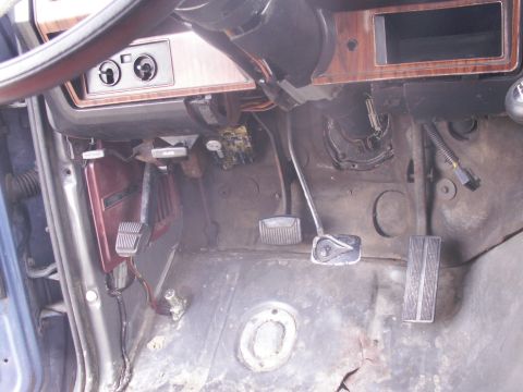 1986 Ford Bronco - The interior of a vehicle shows the floor pedals and lower dashboard area, with visible wiring and trim.