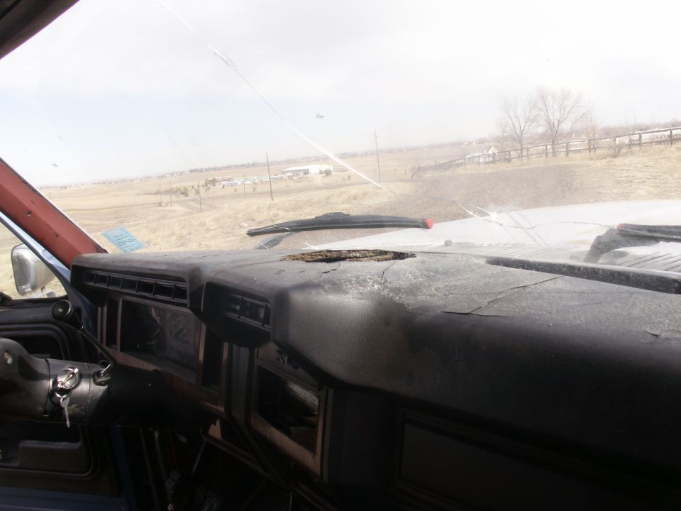 Dashboard interior of a weathered vehicle, showing cracked dashboard, steering wheel, and a view through the windshield
