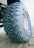 1988 Ford Bronco - A close-up view of a large, aggressive tread tire, likely for off-road use, resting on a sandy surface.