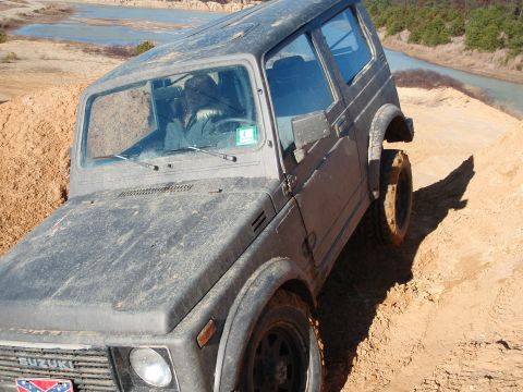 1987 Suzuki Samurai - A Suzuki Samurai is shown navigating a sandy incline with a water feature in the background.