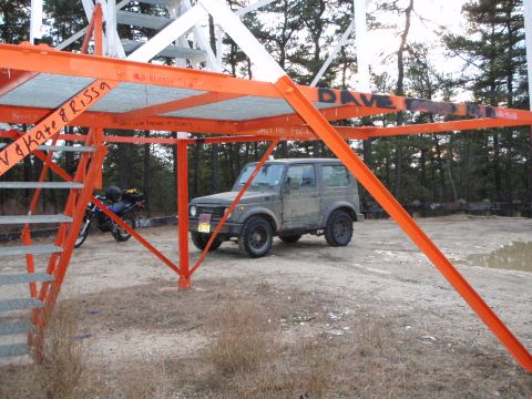 1987 Suzuki Samurai - A 1987 Suzuki Samurai is parked beneath a metal structure, with a motorcycle visible to the left.
