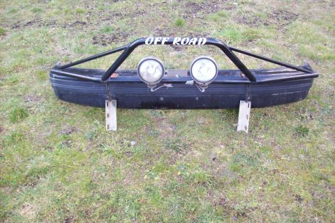 1995 Ford Bronco - Aftermarket off-road bumper with "OFF ROAD" lettering and auxiliary lights, mounted on wooden supports.