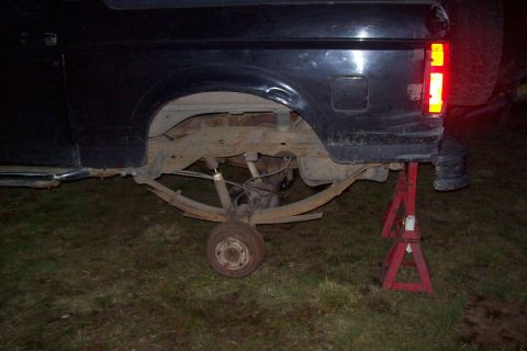 1995 Ford Bronco - The rear suspension of a black Ford Bronco is visible, with one wheel removed and the vehicle supported by jack stands.
