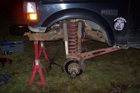 1995 Ford Bronco - The front suspension of a Ford Bronco is visible while it's supported by jack stands.