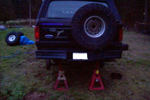 1995 Ford Bronco - Rear view of a black Ford Bronco, supported by red jack stands, with a spare tire on the tailgate.