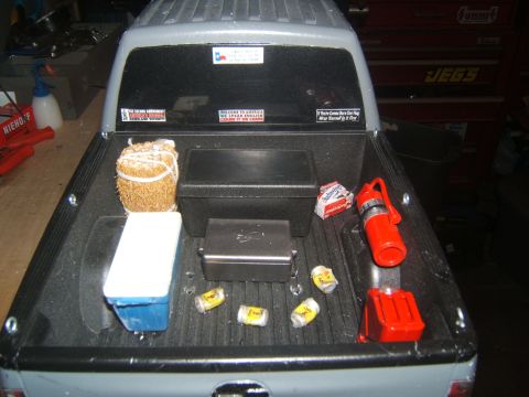 1988 Ford Bronco - The bed of a pickup truck is filled with various items including a cooler, a bundle of hay, toolboxes, a fire extinguisher, and several can…