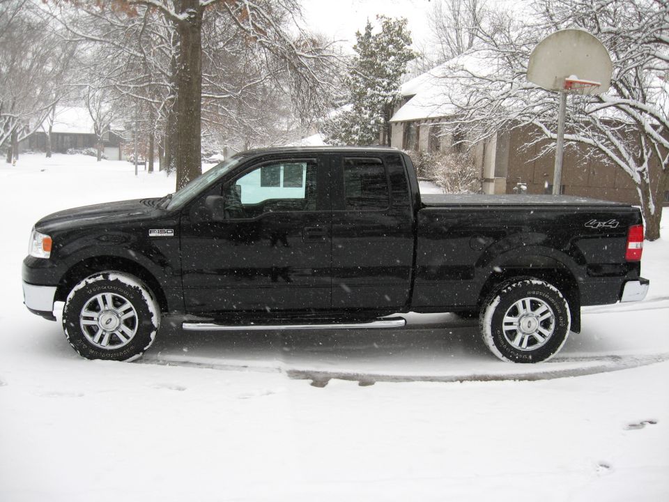 Black Ford F-150 pickup truck in the snow, side view.