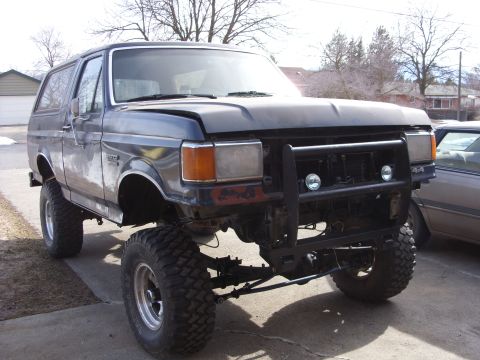 1988 Ford Bronco - A lifted, dark gray 1988 Ford Bronco with large off-road tires sits in a driveway. The front bumper has been replaced with a black brush gu…