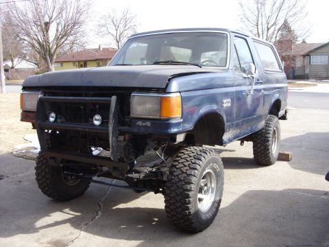 1988 Ford Bronco - A blue Ford Bronco with a custom front bumper and large off-road tires sits in a driveway. The vehicle appears to be undergoing modificatio…