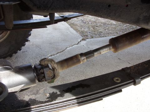 1988 Ford Bronco - A close-up view of a vehicle's driveshaft and U-joint assembly, connected to the differential, with leaf springs visible below.