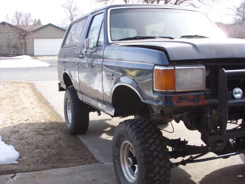 1988 Ford Bronco - A dark blue Ford Bronco is parked on a paved surface with a residential background. The vehicle is lifted with large off-road tires and sho…