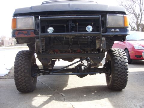1988 Ford Bronco - The front view of a lifted, dark-colored truck with large off-road tires and a custom brush guard. The vehicle appears to be undergoing mod…