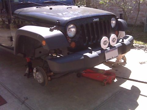 2008 Jeep Wrangler - A dark colored Jeep Wrangler is shown with its front end raised on a red hydraulic jack and a jack stand. The front bumper has two round He…