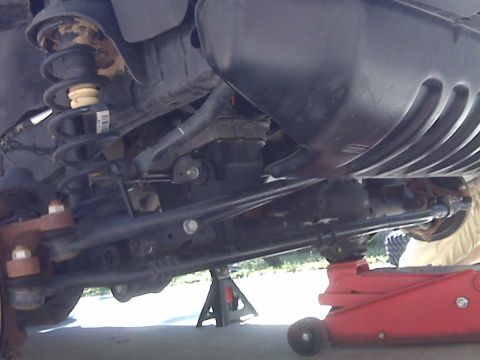 2008 Jeep Wrangler - The underside of a 2008 Jeep Wrangler is shown, supported by a red hydraulic jack and a jack stand. The suspension components, including th…